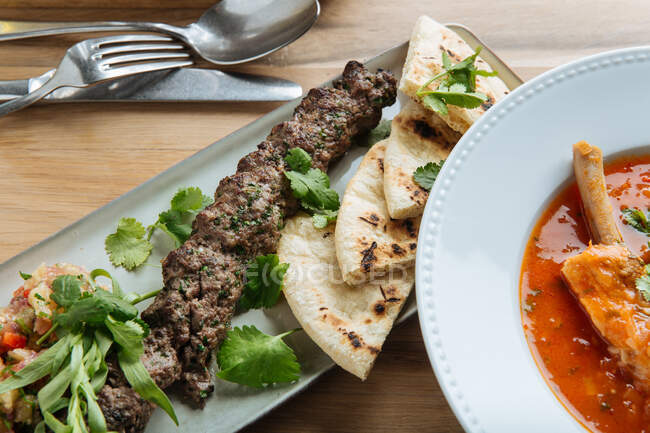 Vista superior da sopa vermelha com carne e ervas frescas na mesa de madeira com kebab e pão liso no restaurante — Fotografia de Stock