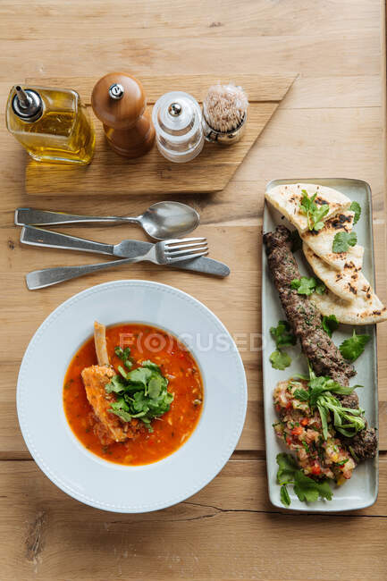 Top view of red soup with meat and fresh herbs on wooden table with kebab and flat bread in restaurant — Stock Photo