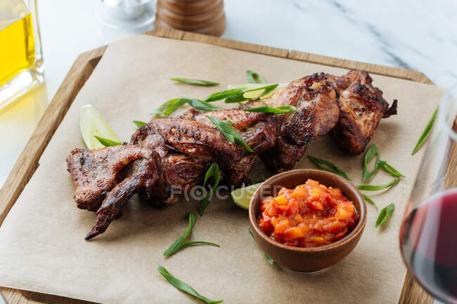 From above of grilled chicken wings on wooden board with slices of lime herbs and red sauce — Stock Photo