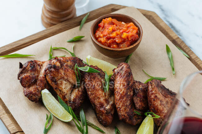Von oben gegrillte Chicken Wings auf Holzbrett mit Limettenscheiben und roter Soße — Stockfoto