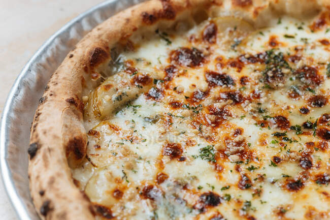 Сверху сочная запечённая пицца подается с сыром и травами на столе в ресторане — стоковое фото