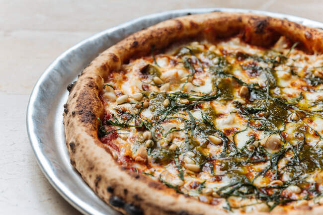 Desde arriba de jugosa pizza vegetariana al horno servida con queso, semillas y hierbas en la mesa en el restaurante - foto de stock