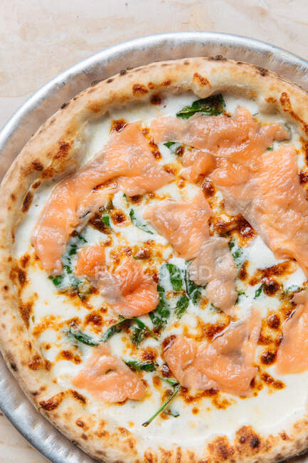 Vista dall'alto della pizza fresca al forno con formaggio e fette di pesce rosso decorate con erbe aromatiche nel ristorante — Foto stock