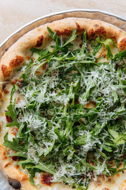 Primo piano dall'alto di gustosa pizza al forno decorata con rucola verde e formaggio grattugiato nel ristorante — Foto stock