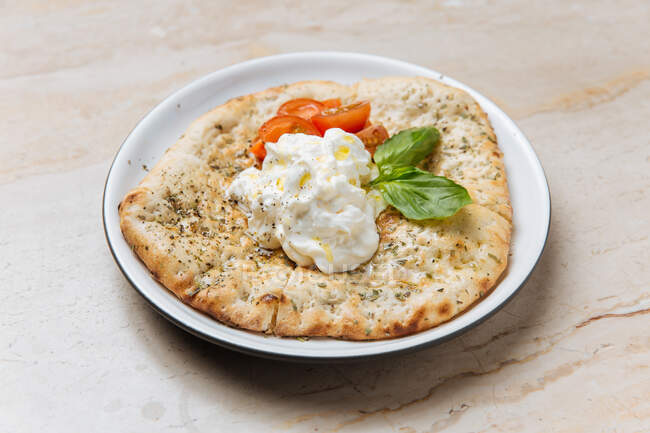 From above of baked golden dough served with creamy sauce slices of tomato and basil leaves in restaurant — Stock Photo