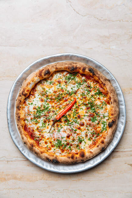 Вид зверху круглої піци з томатним соусом і розтопленим сиром, прикрашеним подрібненим зеленим і одиночним кайенським перцем — стокове фото