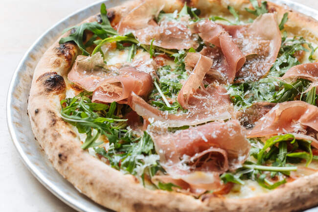 Blick von oben auf leckere Pizza mit dünnen Speckscheiben und frischem Grün auf dem Teller im Restaurant — Stockfoto