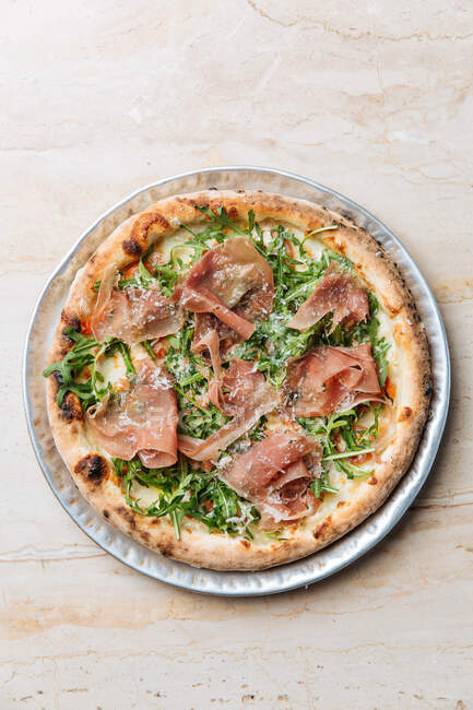 Верхний вид вкусной пиццы с тонкими ломтиками бекона и свежей зелени на тарелке в ресторане — стоковое фото