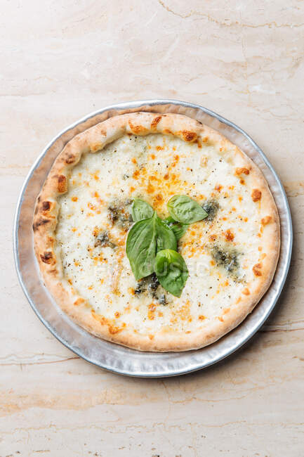 From above of juicy baked pizza served with cheese and basil herbs on table in restaurant — Stock Photo