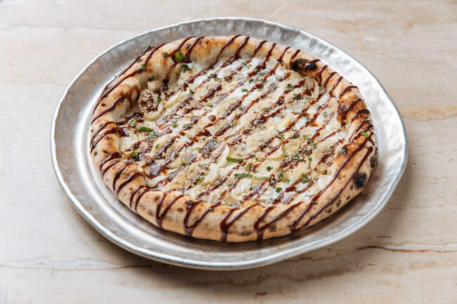 From above of crispy pizza with thick edge filled with bananas and topped with crushed nuts and chopped mint drizzled with chocolate sauce — Stock Photo