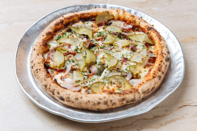 Vista superior de pizza redonda con queso mozzarella derretido rematado con rodajas rojizas y cebolla con encurtidos - foto de stock