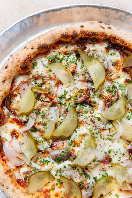 Вид сверху на круглую пиццу с расплавленным сыром моцарелла, увенчанным нарезанным красноватым и луком с огурцами — стоковое фото