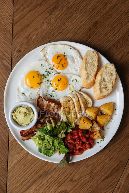 Vista superior do pequeno-almoço inglês servido com ovos fritos e bacon com torradas e legumes em mesa de madeira — Fotografia de Stock