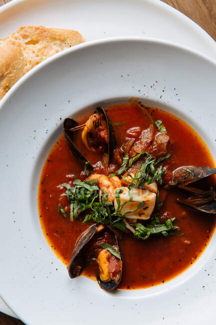 Draufsicht auf weißen runden Teller mit reicher würziger Tomatensuppe mit schwarzen Miesmuscheln und Meeresfrüchten garniert mit gehacktem Gemüse — Stockfoto