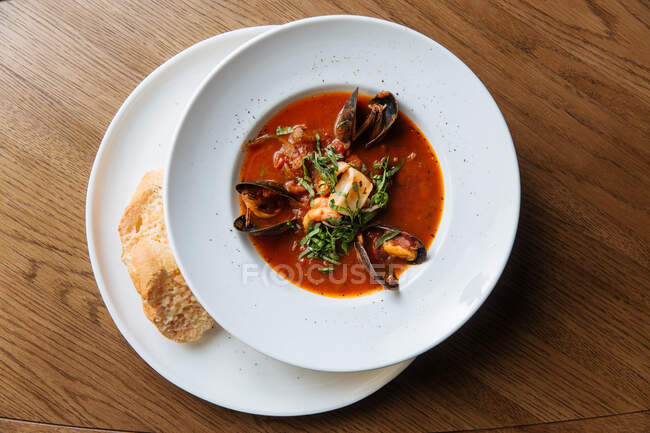 Top view of white round plate with rich spicy tomato soup with black mussels and seafood garnished with chopped greens — Stock Photo