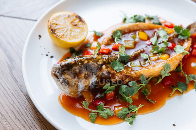 De cima de todo o peixe branco assado cortado e preenchido com molho de tomate e legumes decorados com coentro verde — Fotografia de Stock