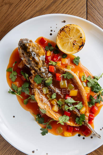 From above of whole roasted white fish cut and filled with tomato sauce and vegetables garnished with green cilantro — Stock Photo