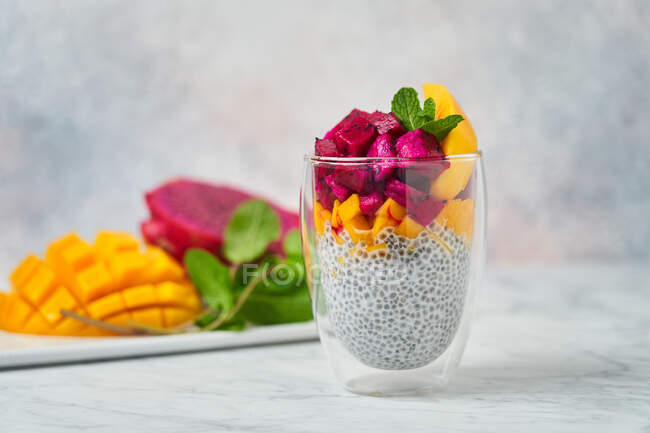 Pouding au chia décoré avec des tranches de pitaya rouge mangue et menthe fraîche en verre avec des ingrédients frais sur fond flou — Photo de stock