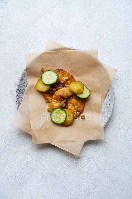 Vue du dessus de la sauce dorée sur une assiette avec du papier cuisson décoré de tranches de concombres verts frais et marinés sur la table — Photo de stock