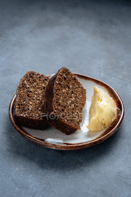From above of slices of rye bread with bran on plate with slice of butter on grey table — Stock Photo