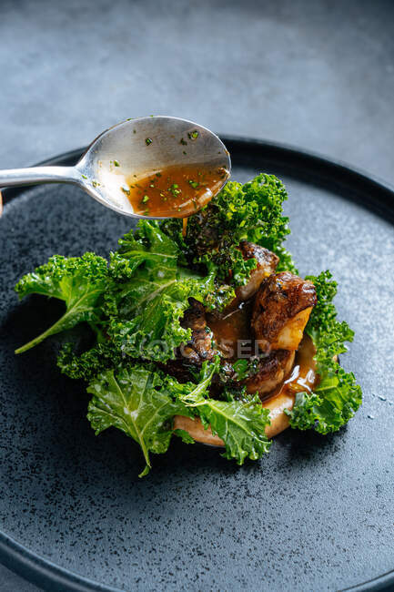 Сверху жареное мясо подается со свежими зелеными листьями салата на черной тарелке, надуваясь коричневым соусом с ложкой — стоковое фото
