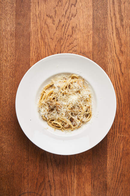 Vista superior de plato blanco con espaguetis cocidos y queso rallado sobre mesa de madera - foto de stock