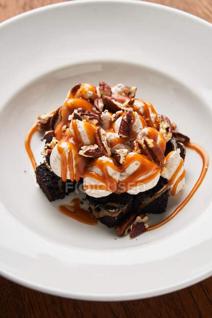 From above of slices of brownies with white ice cream and pieces of chocolate served with caramel on white plate — Stock Photo