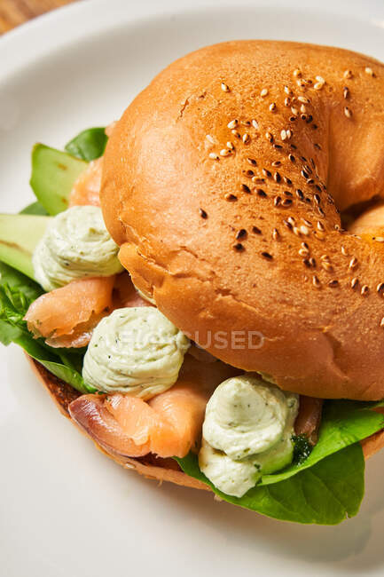 From above of red salmon meat and fresh green basil leaves with creamy sauce under soft baked bun with sesame on plate — Stock Photo