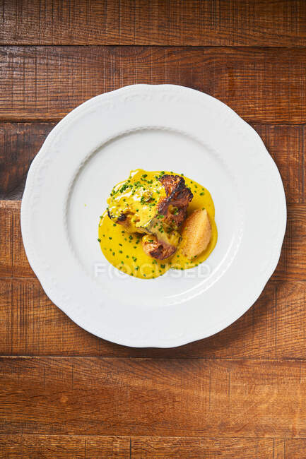 Draufsicht auf gegrilltes Fleisch auf weißem Teller, gelbe dicke Soße mit Kräutern auf Holztisch im Restaurant — Stockfoto