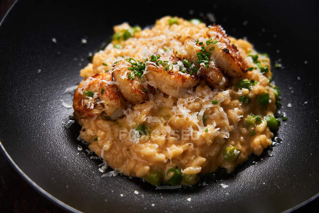 Von oben Reis in goldener Sauce mit gebratenen Garnelen, geriebenem Käse und grünen Kräutern auf stilvollem schwarzen Teller — Stockfoto