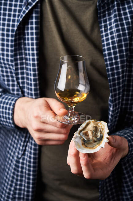 Безликий парень в повседневной одежде с современным стаканом виски и вкусным моллюском в руках — стоковое фото