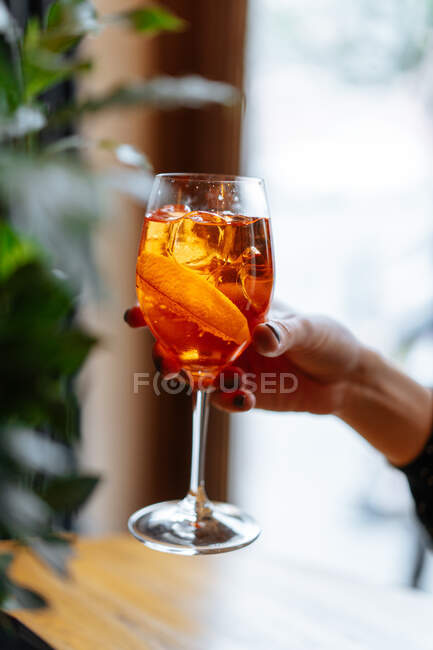 Anonymous woman holding alcohol cocktail with aperol and campari decorated with slices of orange in restaurant — Stock Photo
