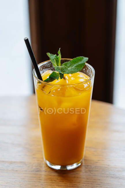 D'en haut de délicieuse boisson jaune en verre highball avec glace décorée de menthe verte fraîche sur table en bois au restaurant — Photo de stock