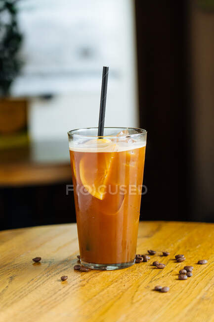 Cold coffee with ice and slices of lemon in modern glass with tube on wooden table with coffee bean — Stock Photo
