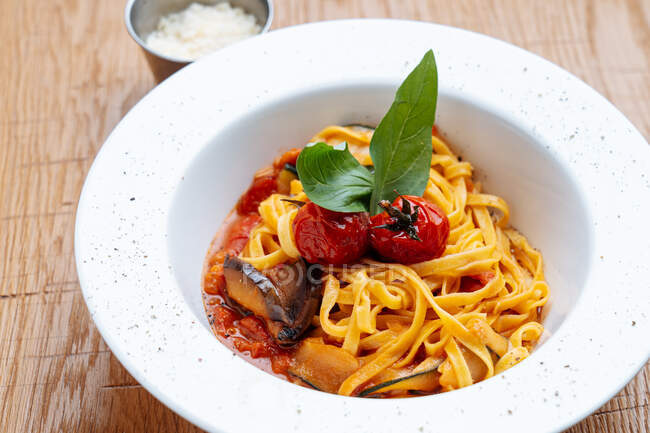 De arriba del plato blanco con los espaguetis con los trozos del calabacín con los tomates cocidos la salsa roja y la hoja de albahaca - foto de stock