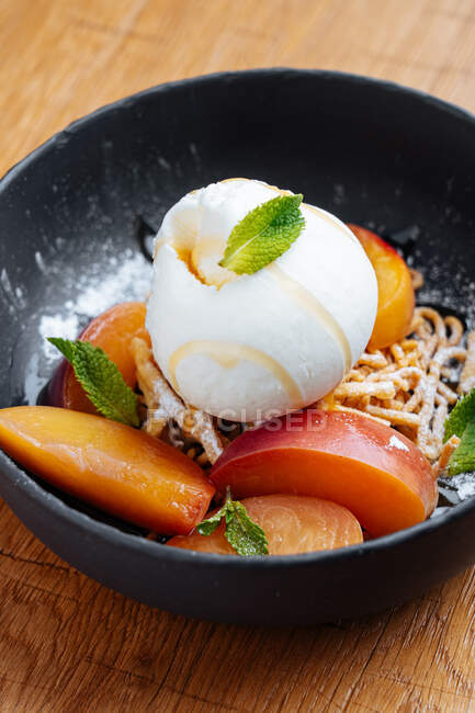 From above of fresh slices of mango with creamy ice cream and sweet spaghetti decorated with mint in stylish black bowl — Stock Photo