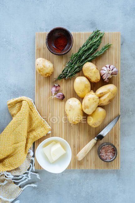 Vue de dessus des pommes de terre propres et de l'assaisonnement frais placés sur la planche à découper près du couteau et de la serviette pendant la préparation du dîner — Photo de stock