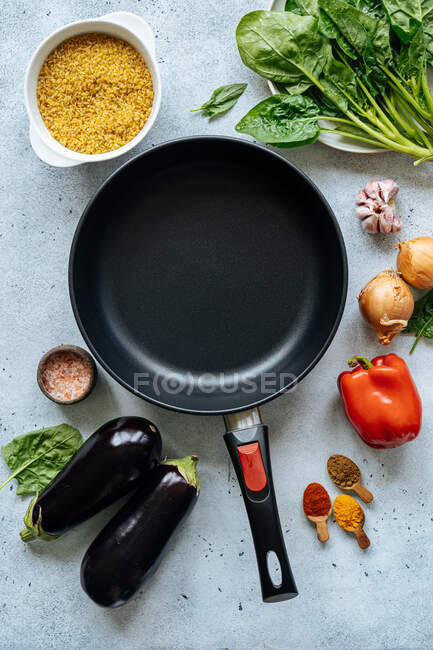D'en haut divers légumes et épices pour la préparation du déjeuner disposés autour de la poêle à frire vide sur la table dans la cuisine — Photo de stock