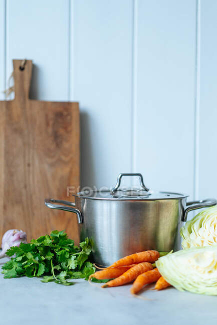 Стиглий капуста і морква розміщені поруч з купою свіжої петрушки і металевого каструлі під час обідньої підготовки на кухні. — стокове фото