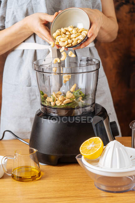 Mulher irreconhecível adicionando caju no liquidificador moderno enquanto prepara prato saudável na cozinha — Fotografia de Stock