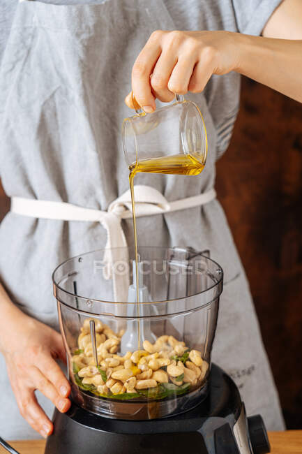 Mulher irreconhecível adicionando óleo ao caju enquanto prepara prato vegan saudável no liquidificador em casa — Fotografia de Stock
