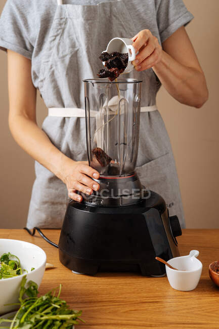 Unerkennbare Weibchen fügen Kochzutat in modernen Mixer ein, während sie zu Hause das Mittagessen zubereiten — Stockfoto