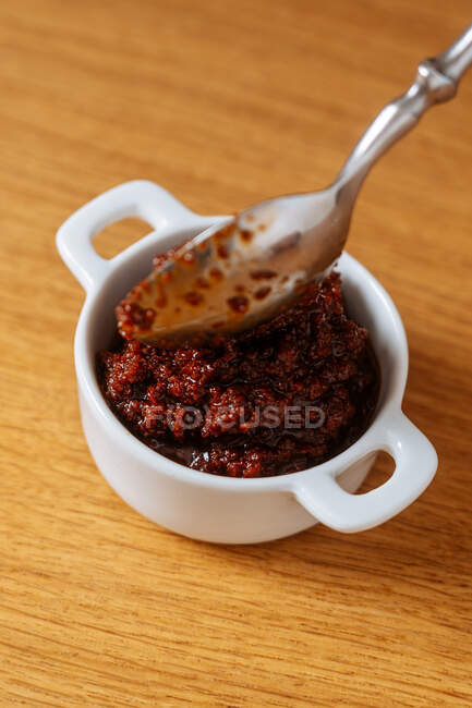 Du dessus cuillère dans un petit bol avec sauce savoureuse sur table en bois dans la cuisine — Photo de stock