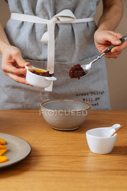 Senhora anônima no avental adicionando molho fresco na tigela enquanto cozinha o almoço na cozinha em casa — Fotografia de Stock