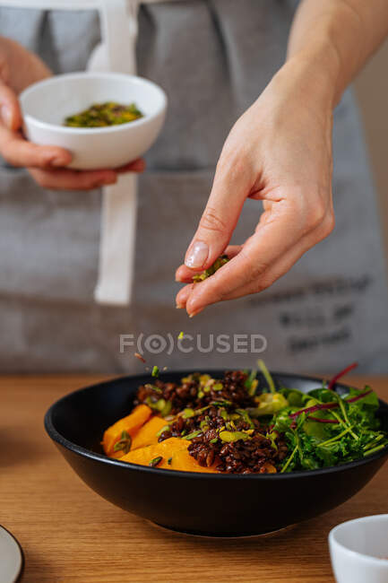 Persona irriconoscibile che aggiunge semi a un piatto vegano sano durante la cottura del pranzo in cucina a casa — Foto stock
