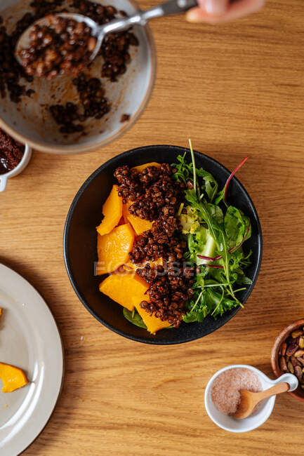 Vista superior da tigela com prato vegan saudável colocado na mesa durante o processo de adição de ingredientes e preparação para o almoço em casa — Fotografia de Stock