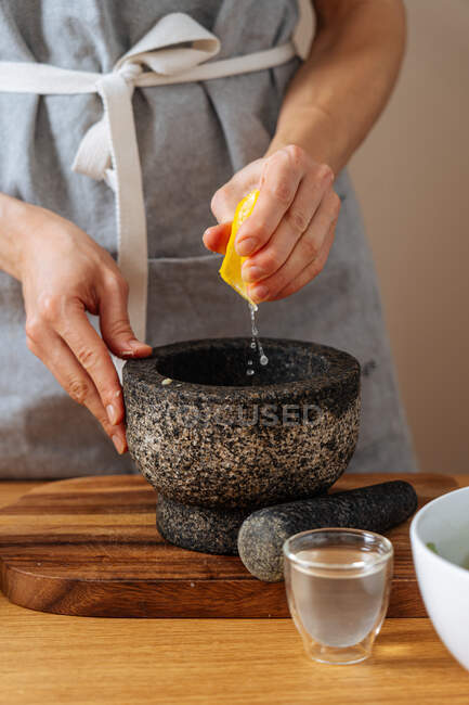 Anonyme Person in Schürze presst Saft frischer Zitrone in Mörser, während sie in der Küche gesunde Gerichte zubereitet — Stockfoto
