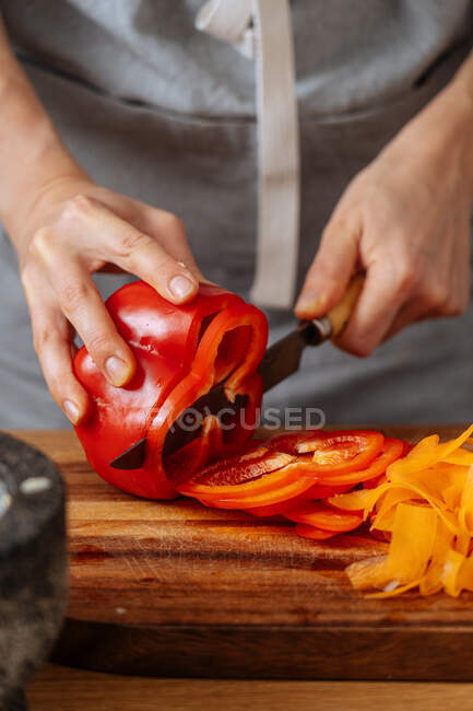 Анонимный человек в фартуке режет свежий перец, готовя здоровый салат к обеду дома — стоковое фото