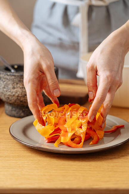 Анонимный человек смешивает нарезанные свежие овощи на тарелке во время приготовления здорового салата дома — стоковое фото