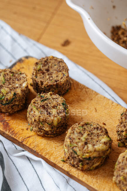 Healthy vegan round raw cutlets made from lentil and zucchini on wooden cutting board placed on wooden table with white striped cloth — Stock Photo